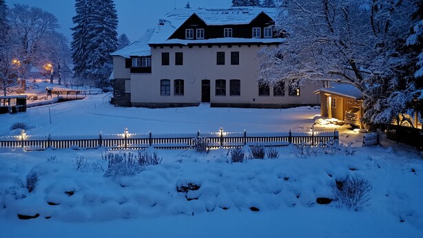 A large, two-story house with a snow-covered roof and yard, surrounded by snow-laden trees. - Penzion Bílá voda (Harrachov)