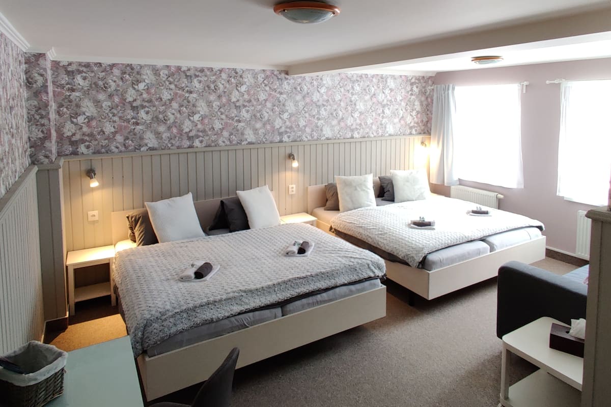 A hotel room with two beds, a small table, a chair, and a window with curtains.