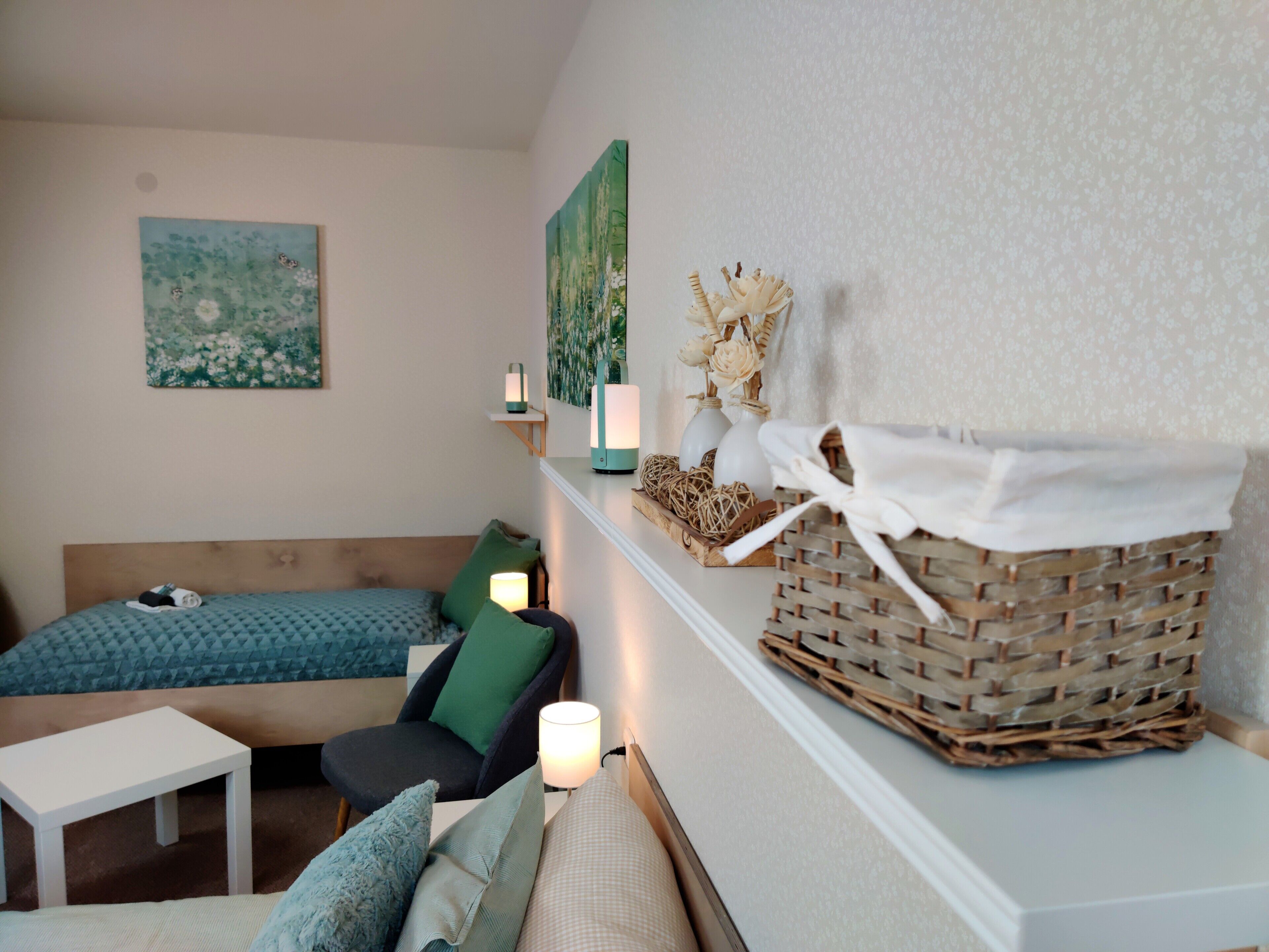 A cozy room with a bed, a chair, a small table, and a shelf with decorative items.