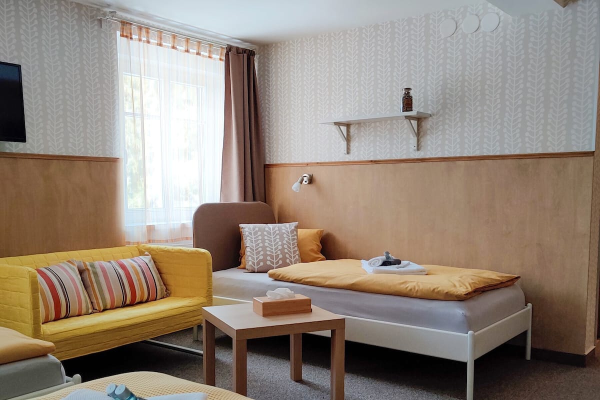 A hotel room with a yellow sofa, a bed with yellow bedding, a small table, and a wall-mounted shelf.