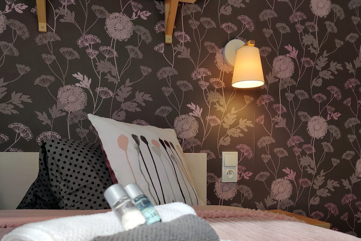 A neatly made bed with a pillow, a rolled towel, and toiletries.