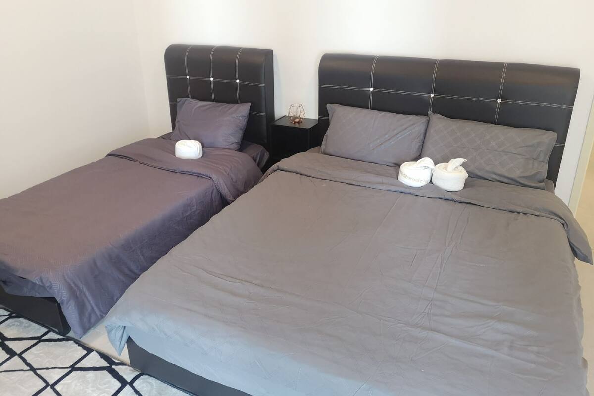 A hotel room with two beds, each with a headboard and pillows. There are two bedside tables with lamps and a small decorative item on one.