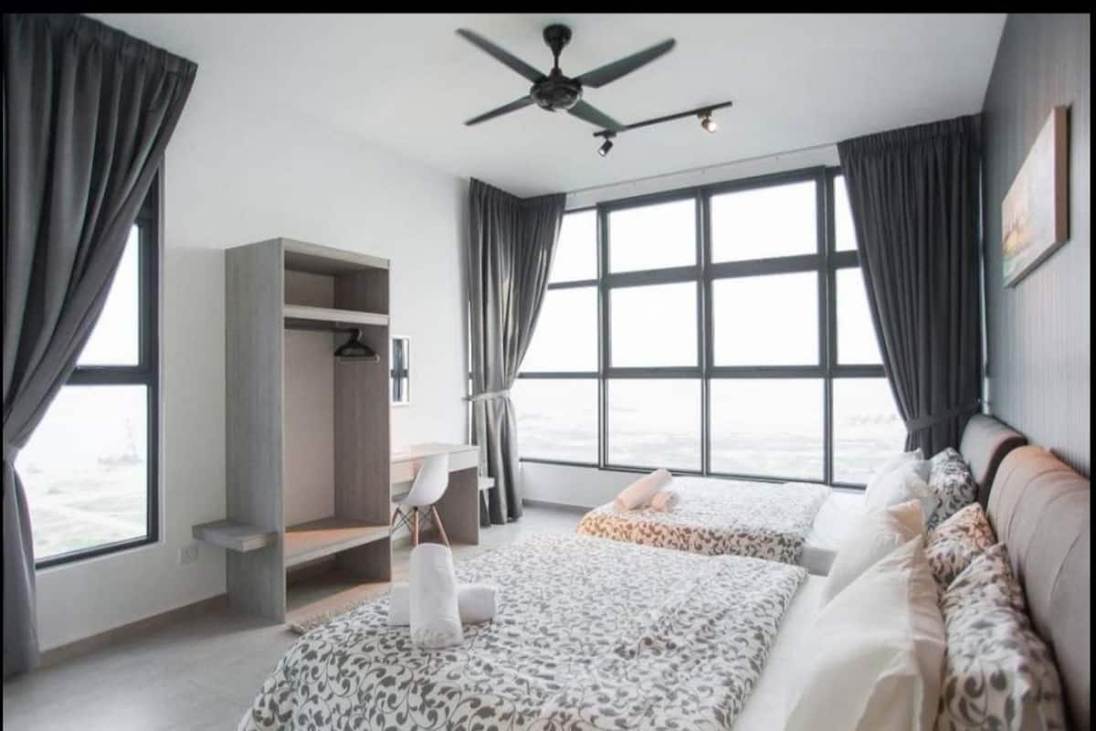 A hotel room with two beds, a desk, a wardrobe, and a large window with curtains.