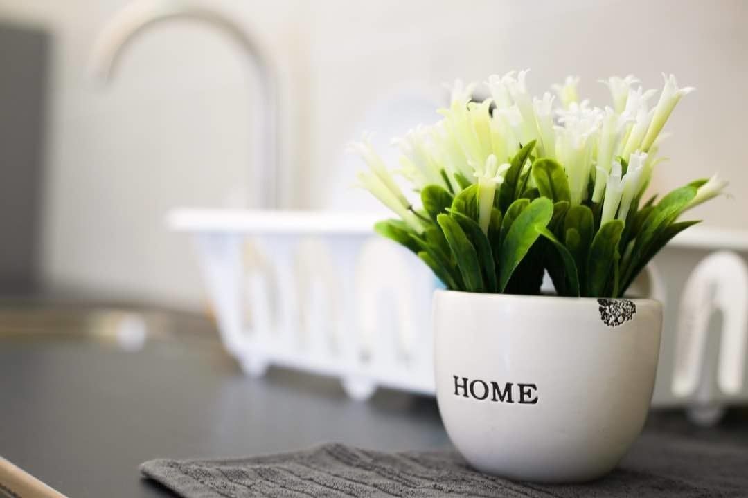 Un pot en céramique blanche sur lequel est inscrit le mot « HOME », placé sur une surface sombre, avec un radiateur blanc en arrière-plan.