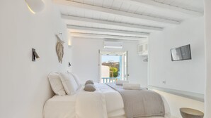 A minimalist bedroom with a bed, a bedside table, a wall-mounted TV, and a view of the outdoors. - Mykonian Mews (Mykonos)
