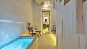 A narrow hallway with a bathtub on the left, a small table with wine glasses and strawberries, and a sofa with patterned cushions. - Mykonian Mews (Mykonos)