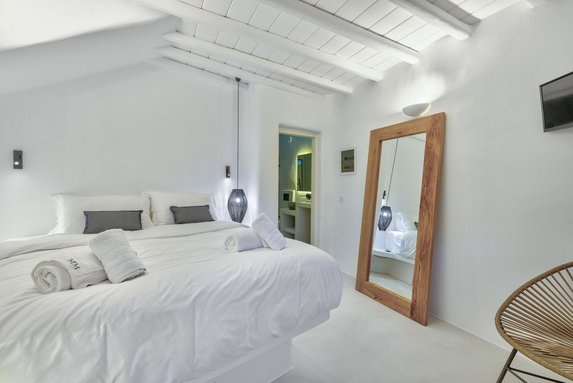 Un dormitorio moderno con una cama grande, un espejo con marco de madera y una silla de mimbre.