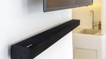 Un baño moderno con un televisor de pared, un estante negro y un lavamanos blanco.