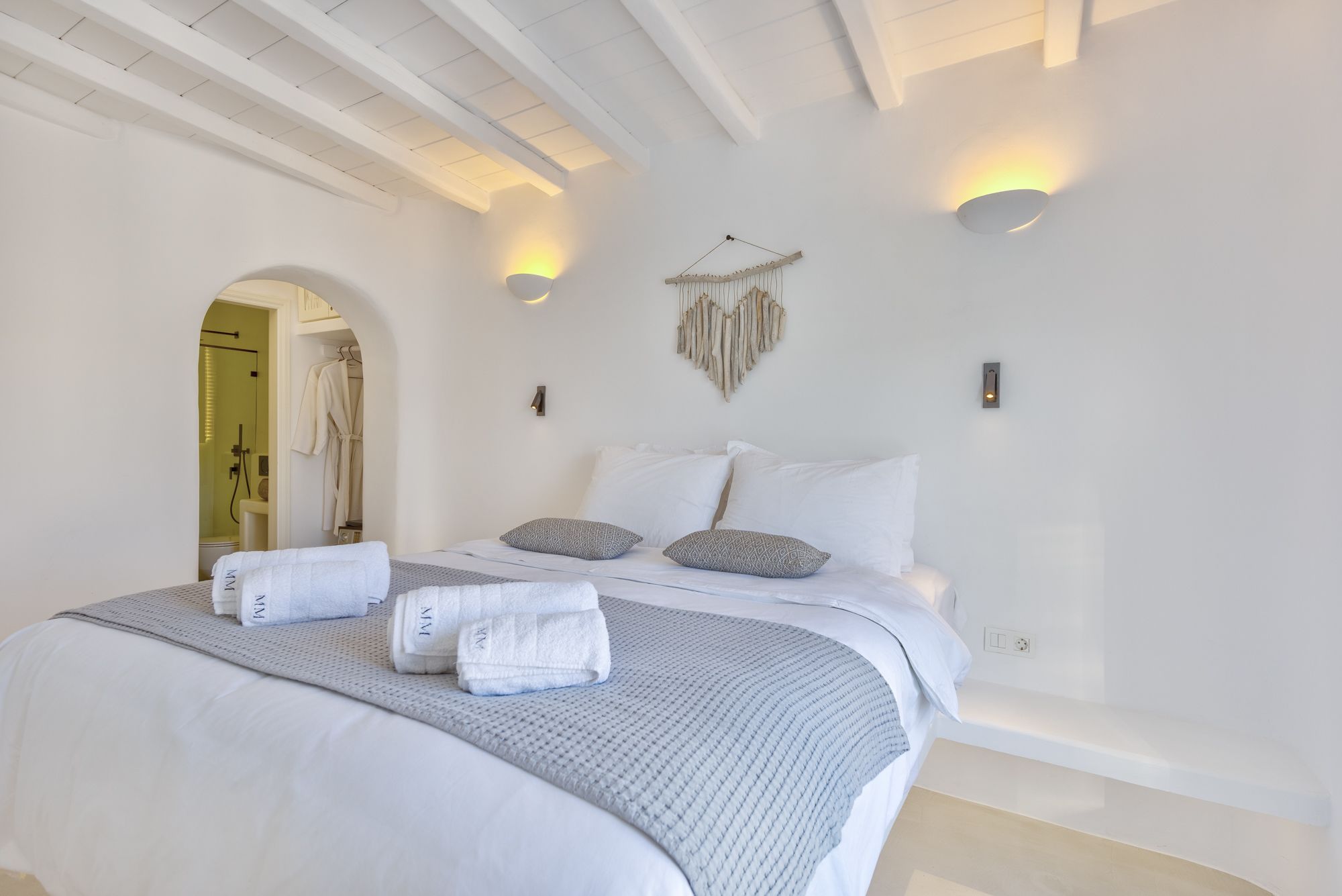 Ein Schlafzimmer mit einem großen Bett, zwei Wandleuchten, einem Wandbild und einer sichtbaren Badezimmertür.
