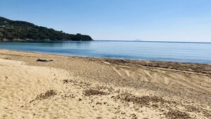 A beach with clear blue water, sandy shore, and a hilly landscape in the background. - Appartamenti La Risacca (Capoliveri)