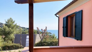 A balcony with a view of the sea, a wooden pergola, and a pink building with shutters. - Appartamenti La Risacca (Capoliveri)
