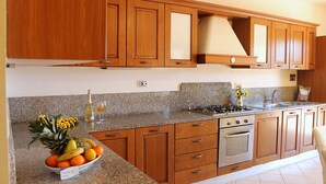 A kitchen with wooden cabinets, granite countertops, a gas stove, an oven, and a bowl of fruit. - Appartamenti La Risacca (Capoliveri)