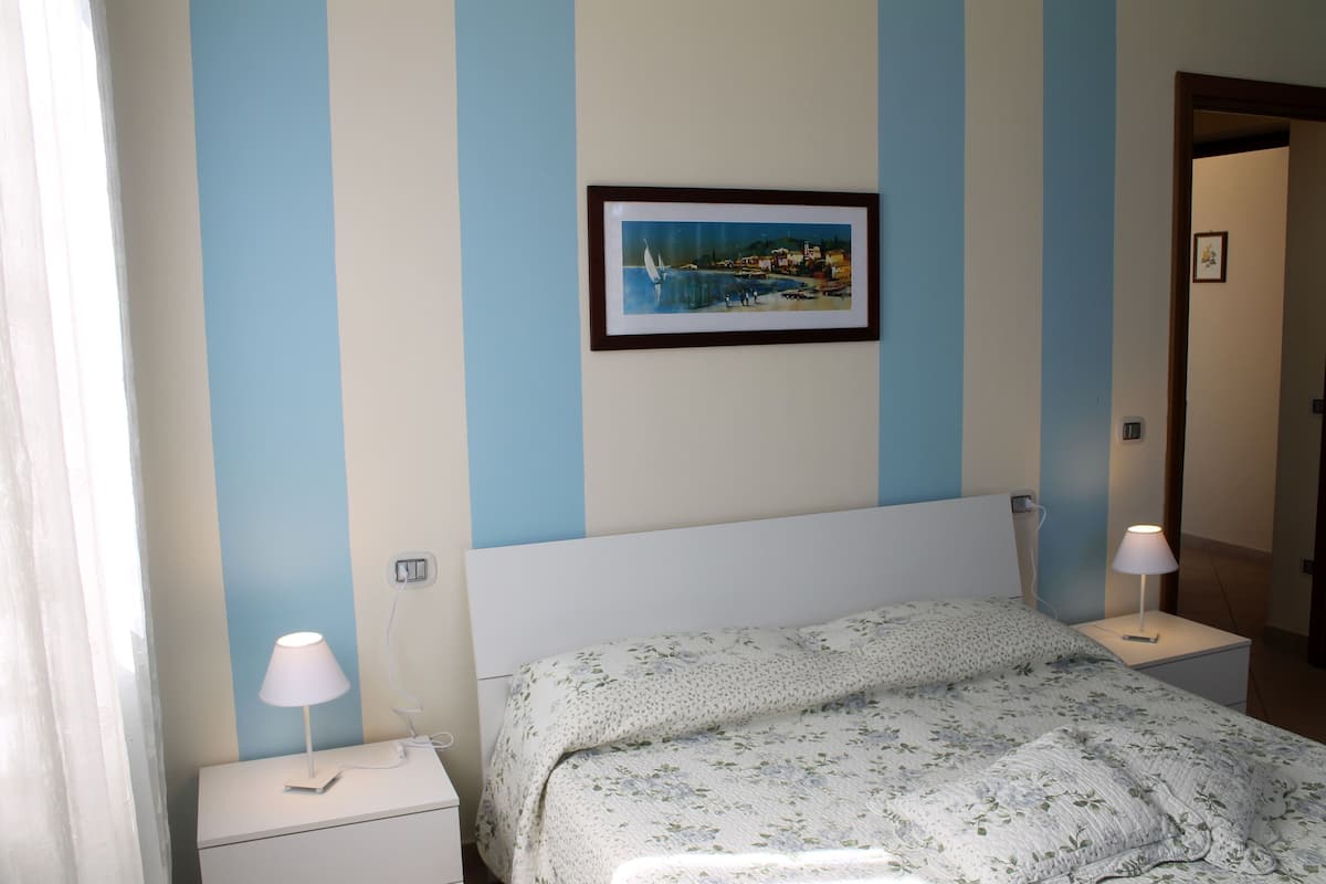 A bedroom with a bed, a nightstand, a lamp, and a framed picture on the wall.