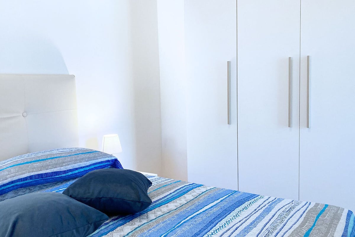 A bedroom with a bed, two pillows, a bedside lamp, and a wardrobe with two doors.