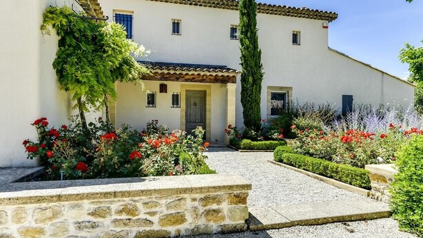 Un edificio de dos pisos con una escalera de piedra que conduce a la entrada, rodeado de jardines cuidados y un camino de grava.