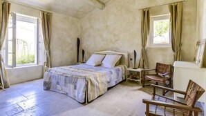 Un dormitorio con cama, dos mesitas de noche, una silla y una ventana con cortinas.