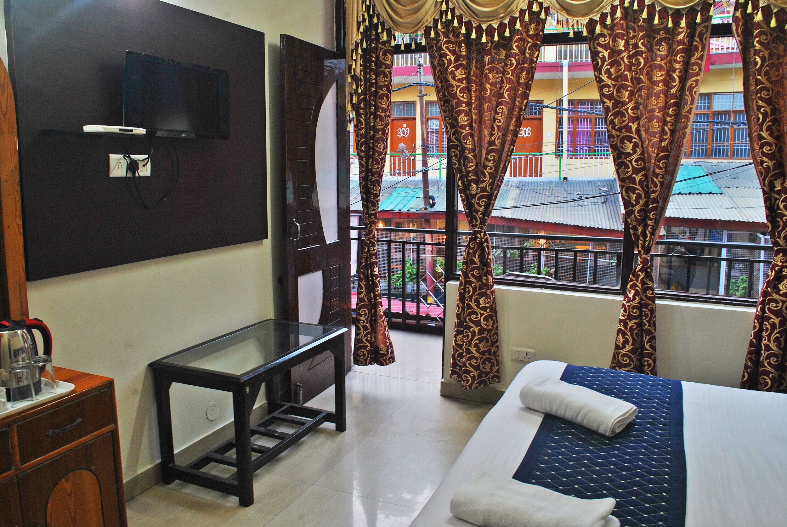 A hotel room with a bed, a TV mounted on the wall, a small table, and curtains.