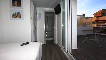 Habitación de hotel con cama, televisor montado en la pared y balcón con mesa y sillas.