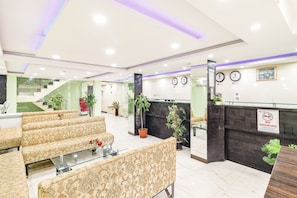 A hotel lobby with patterned sofas, a reception desk, a staircase, and potted plants. - Windsor Castle Inn (Bengaluru)