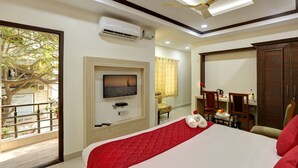 A hotel room with a bed, a TV mounted on the wall, a ceiling fan, and a view of the outdoors. - Windsor Castle Inn (Bengaluru)