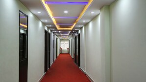 A long, narrow hallway with a red carpet, white walls, and recessed lighting. - Windsor Castle Inn (Bengaluru)
