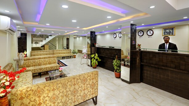 A hotel lobby with patterned sofas, a reception desk, a fireplace, and a staircase. - Windsor Castle Inn (Bengaluru)