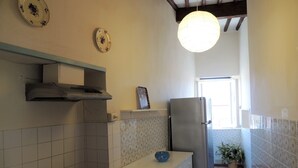 A kitchen with a gas stove, a stainless steel refrigerator, and a hanging light fixture.