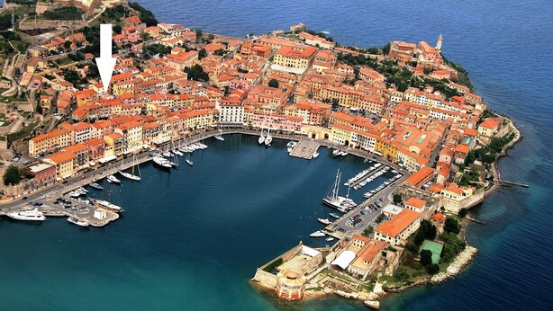 An aerial view of a coastal town with a marina, historic buildings, and a prominent fortification.