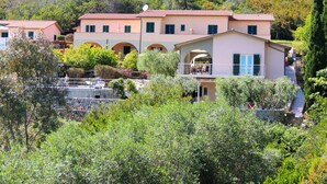 A multi-story building with a central courtyard, surrounded by lush greenery and hills in the background. - Residence Le Solane (Campo nell'Elba)