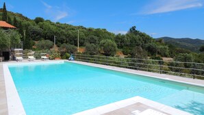 A rectangular swimming pool with a tiled edge, surrounded by a metal railing. There are lounge chairs and a small structure with a red roof in the background. - Residence Le Solane (Campo nell'Elba)