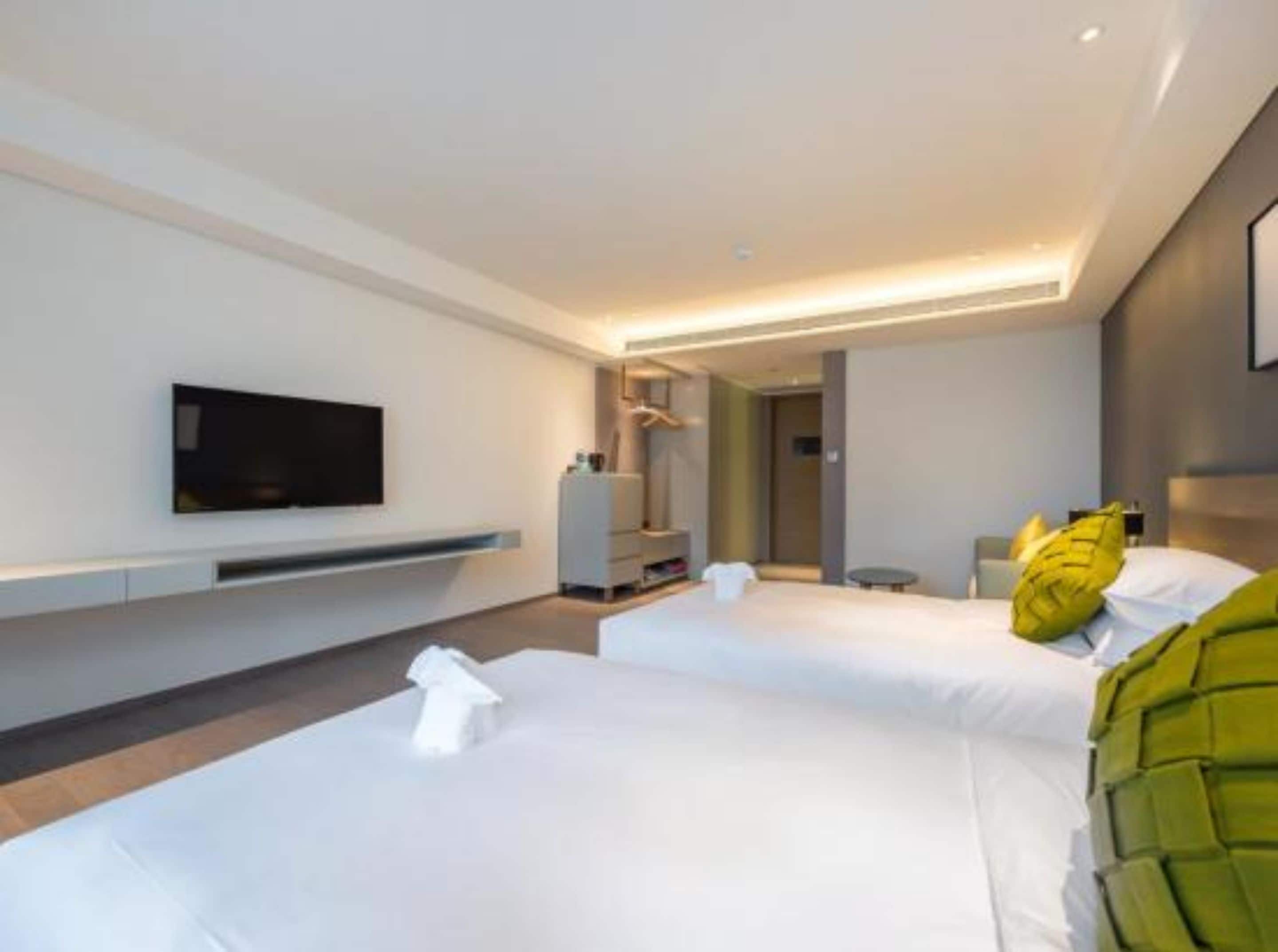 Una habitació d'hotel moderna amb dos llits, un televisor de pantalla plana fixat a la paret i una petita taula de nit.