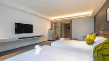 A modern hotel room with two beds, a flat-screen TV mounted on the wall, and a small bedside table.