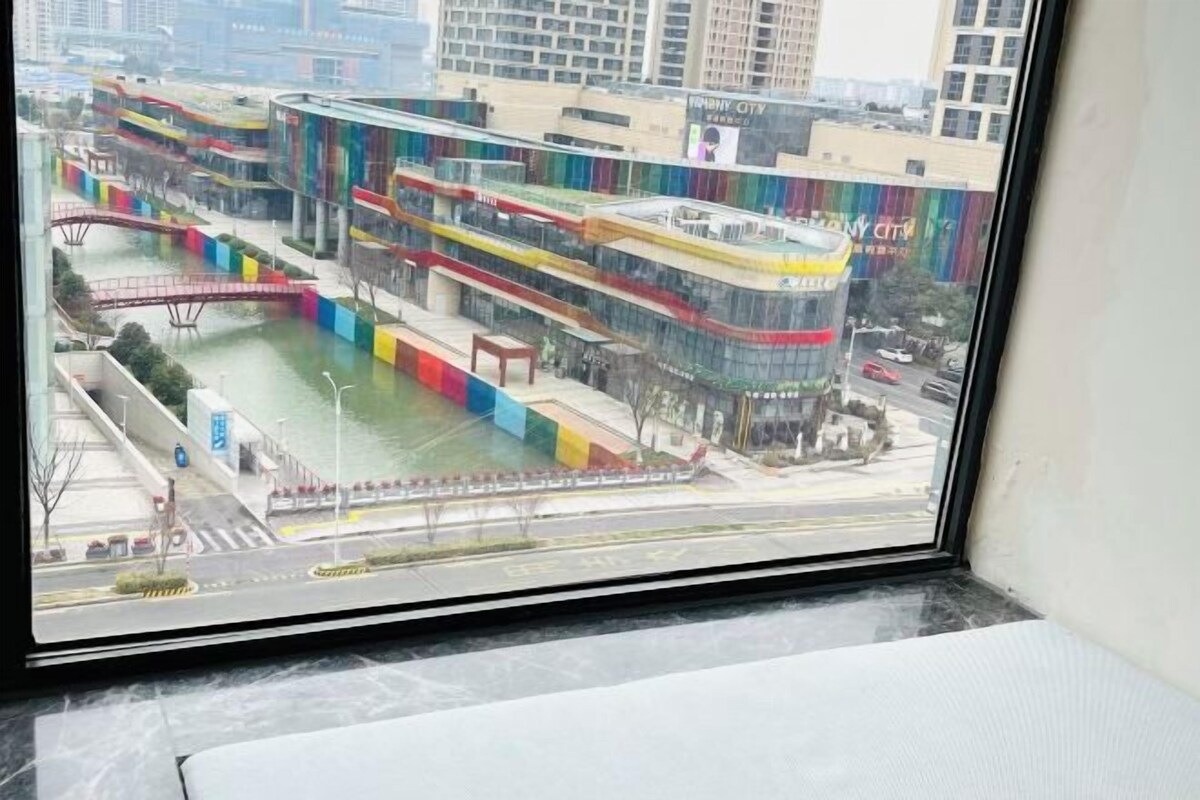 Vista de un edificio moderno con fachada de vidrio, un puente peatonal y una fuente de agua.