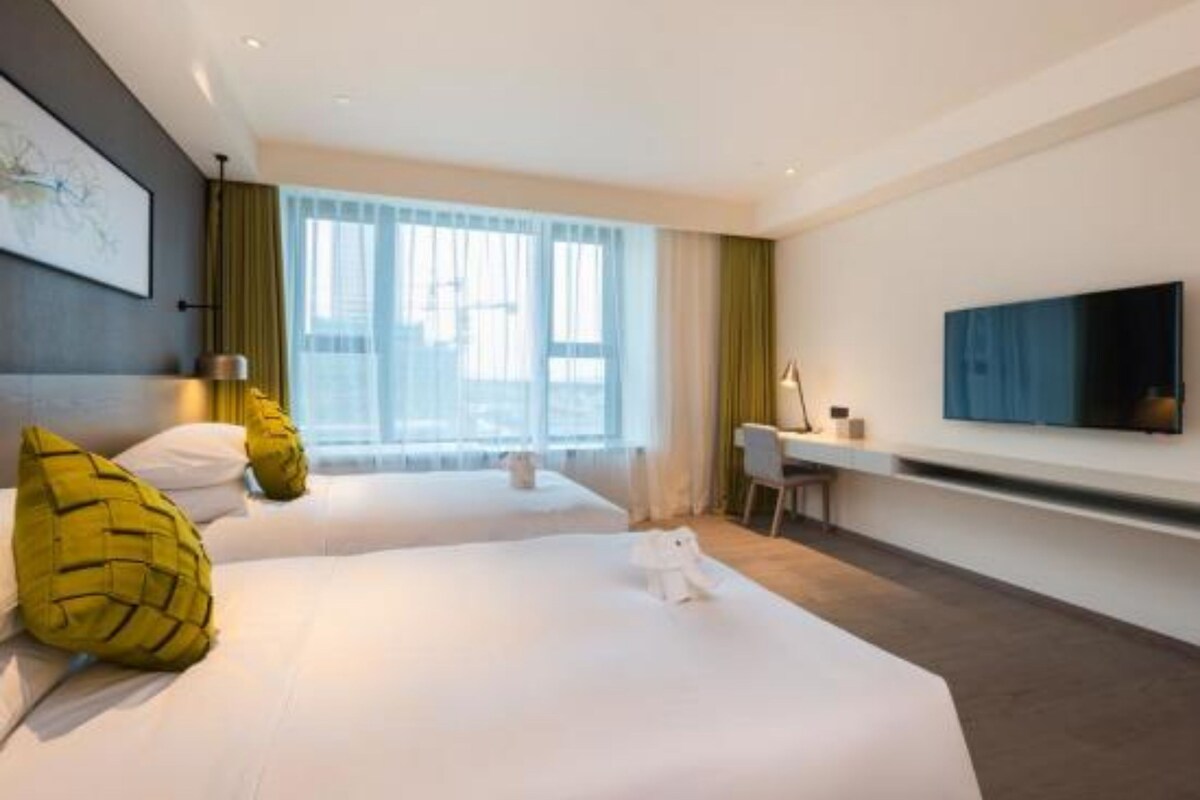 Une chambre d’hôtel avec deux lits, un bureau, une chaise, un téléviseur à écran plat et une grande fenêtre avec des rideaux.