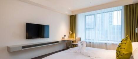 Una habitació d'hotel moderna amb un llit gran, una televisió de pantalla plana penjada a la paret, un escriptori amb una làmpada i una finestra ampla amb cortines.