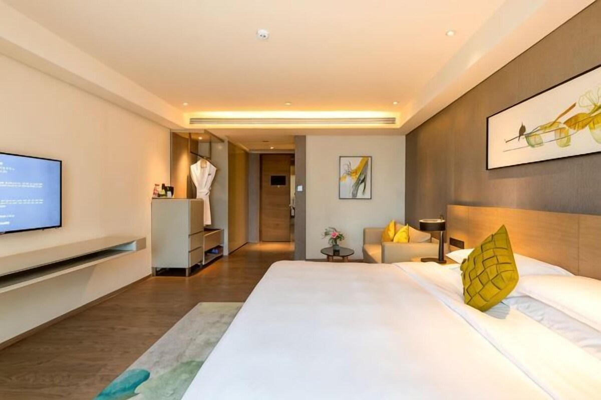 Una habitación de hotel moderna con una cama grande, un televisor de pantalla plana, un vestidor y un baño visible a través de una puerta abierta.