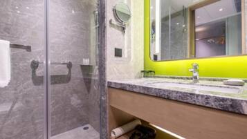 A modern bathroom with a glass shower enclosure, a marble-tiled floor, a wooden vanity with a sink, and a mirror with a green accent wall.