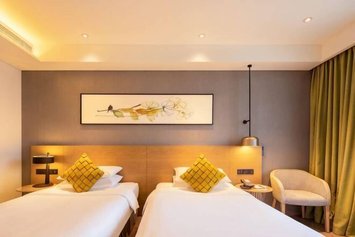 Une chambre d’hôtel avec deux lits, un bureau, une chaise, une lampe et un tableau au mur.