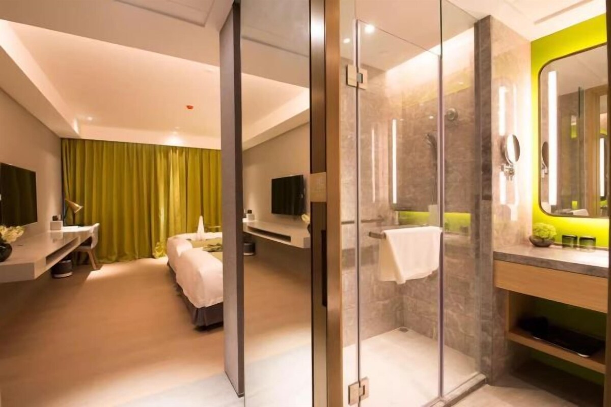 Een moderne hotelkamer met een douchecabine van glas, een bed, een kaptafel met spiegel en een televisie.
