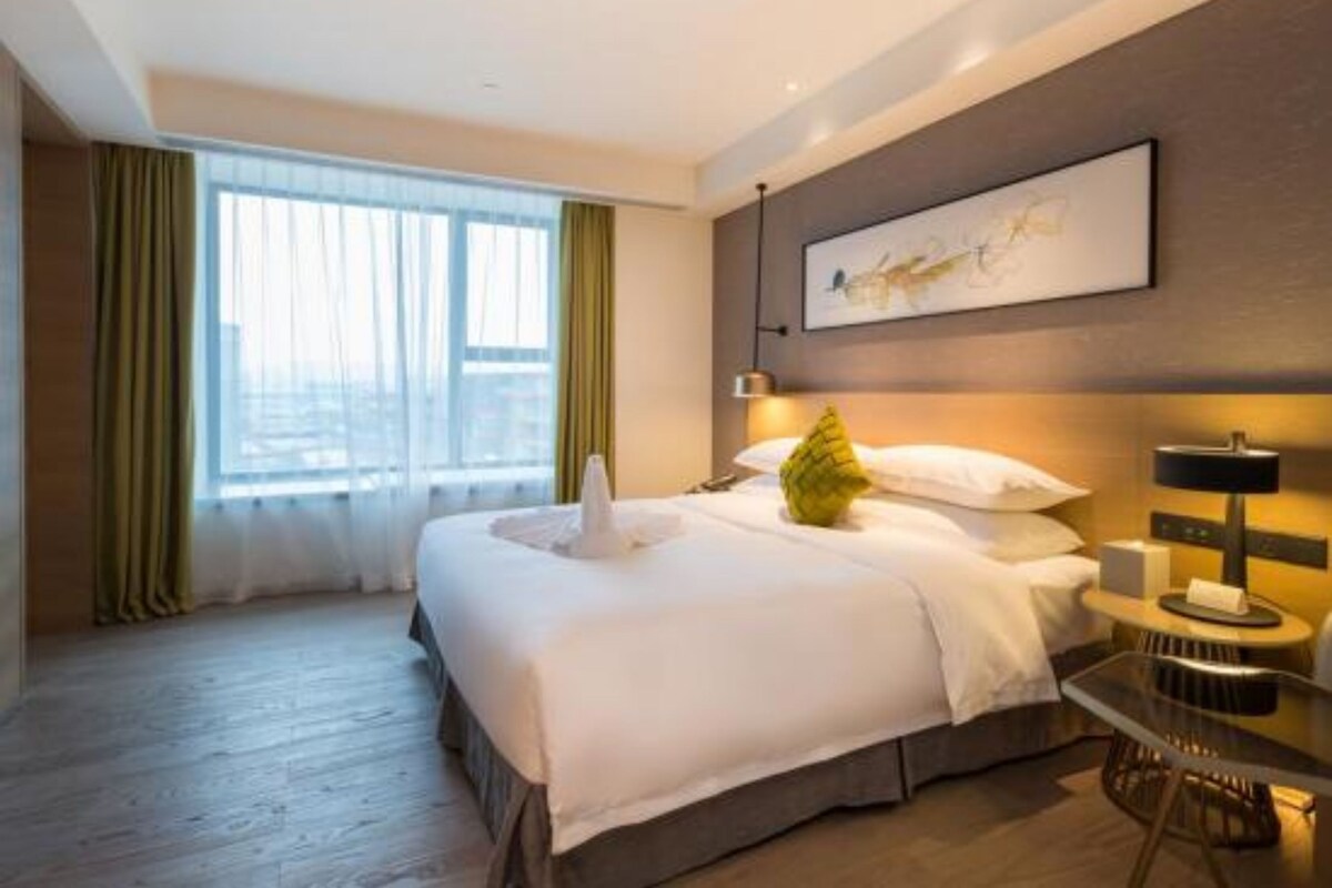 Une chambre d’hôtel moderne avec un grand lit, une table de chevet avec une lampe et une fenêtre avec des rideaux.