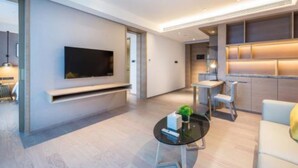 A modern living room with a flat-screen TV mounted on the wall, a glass coffee table with a plant, and a seating area with a sofa and chairs. - The Mulian Hotel Suzhou Branch (Suzhou)