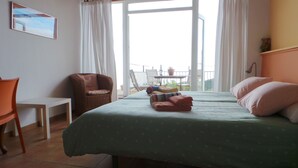 Een kamer met een bed, een stoel, een kleine tafel en een balkon met uitzicht.