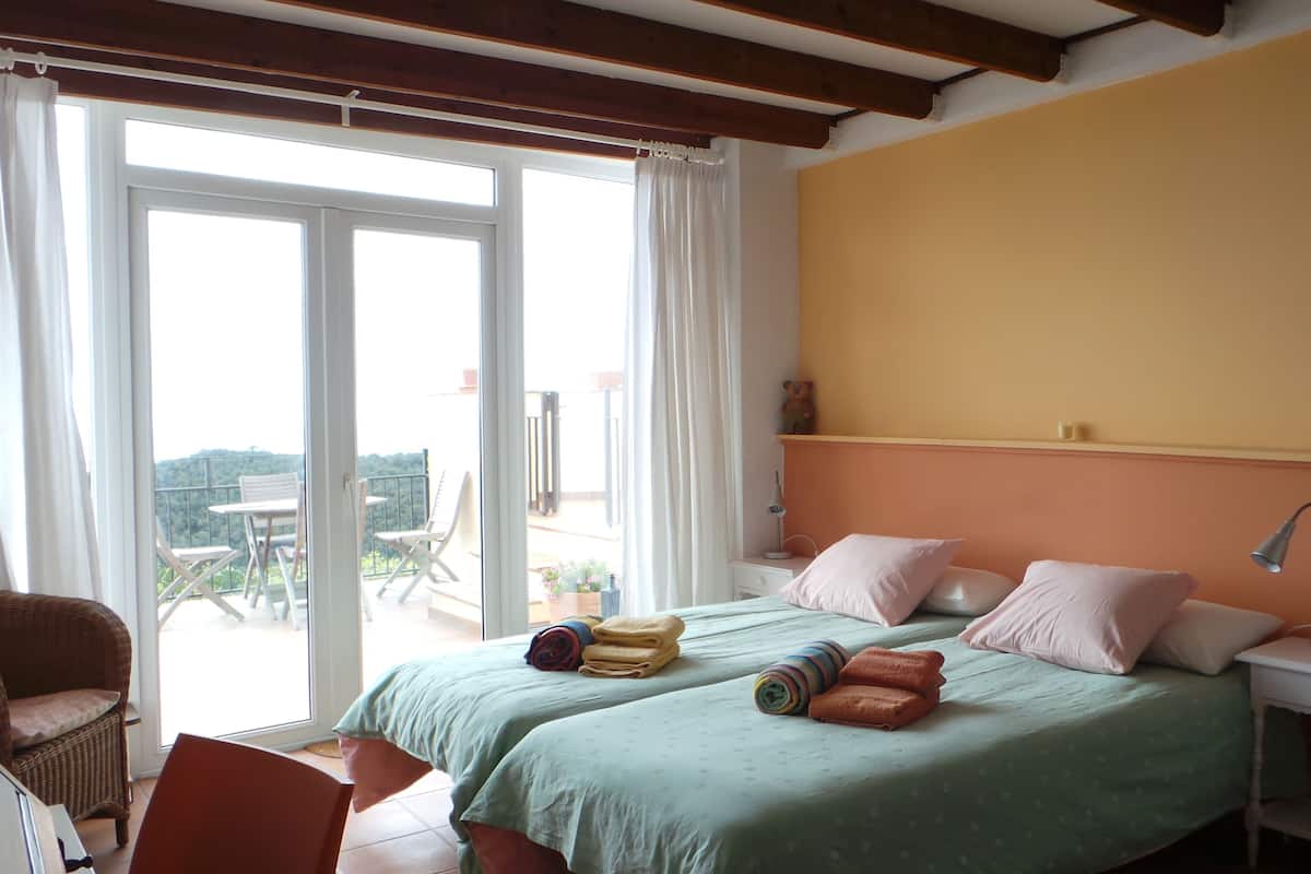 Une chambre avec deux lits, un balcon avec des chaises et une vue sur l’extérieur.