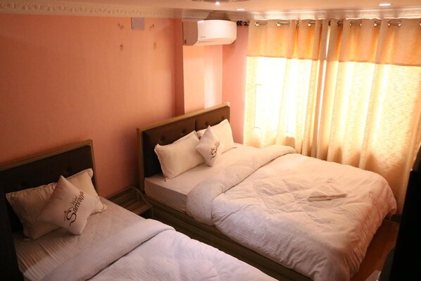 A hotel room with two beds, a ceiling fan, and a window with curtains.