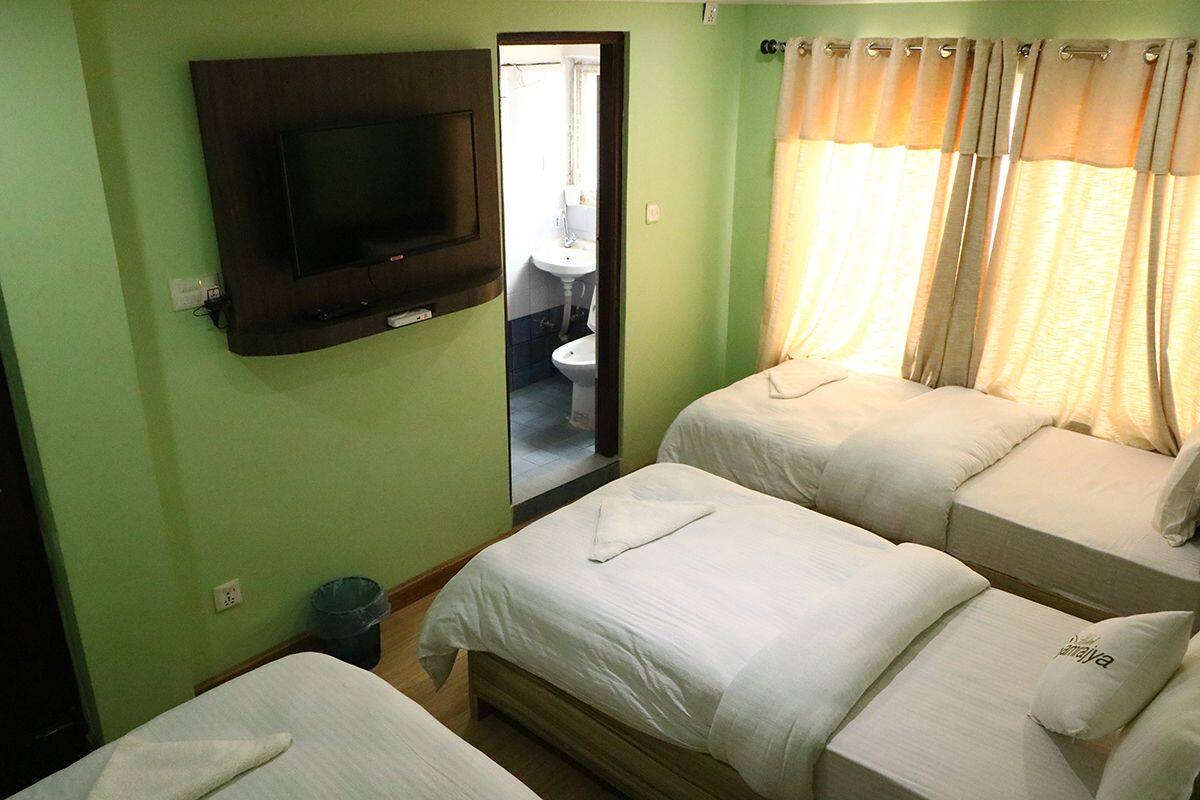 Habitación de hotel con dos camas, un televisor montado en la pared, un baño visible a través de una puerta abierta y una ventana con cortinas.