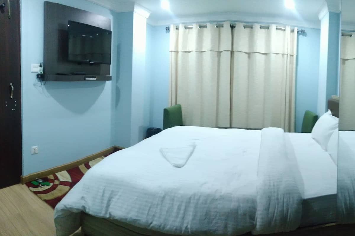 Una habitación de hotel con cama, cortinas, televisor montado en la pared y una puerta.