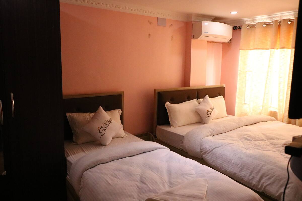 Dos camas individuales con cabeceras, aire acondicionado de pared y ventana con cortinas.