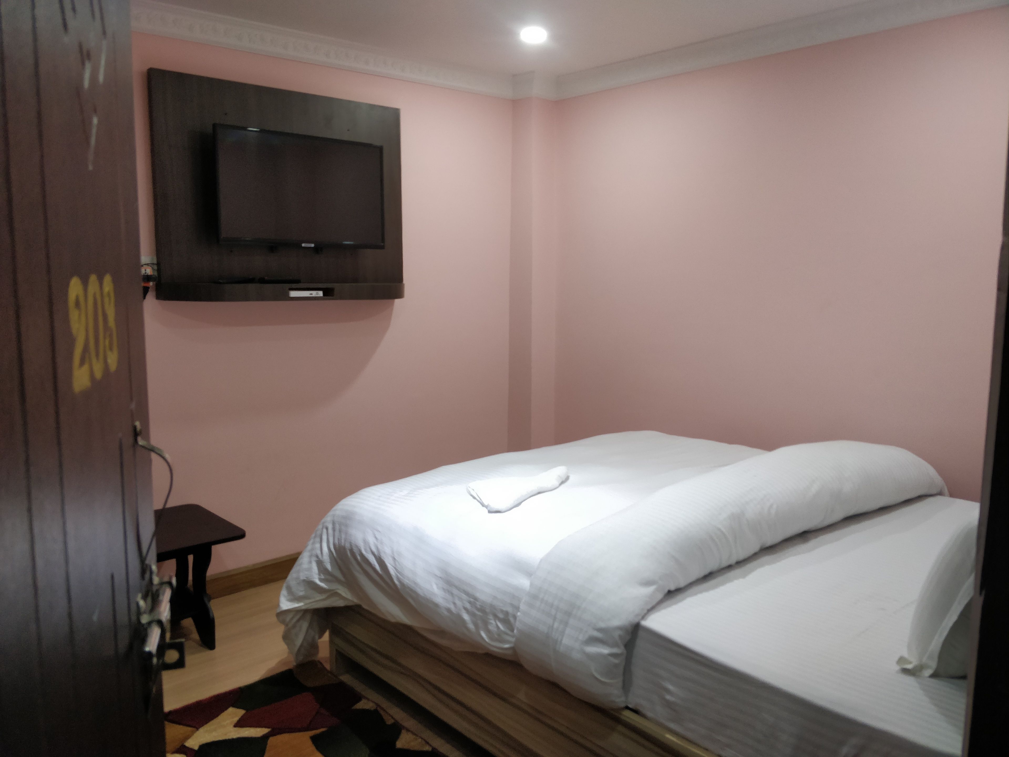 A hotel room with a bed, a TV mounted on the wall, and a small table.