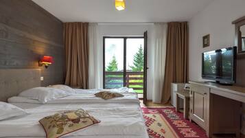Habitación de hotel con cama, escritorio con televisor, ventana con cortinas y vista a árboles.