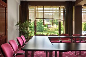Une salle de conférence avec une longue table et des chaises, de grandes fenêtres avec des rideaux et une vue sur un jardin.